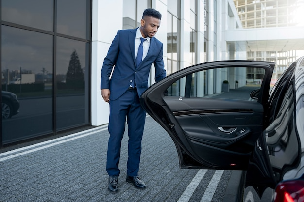Man in blue suit opens a black car door. Driver Leman.